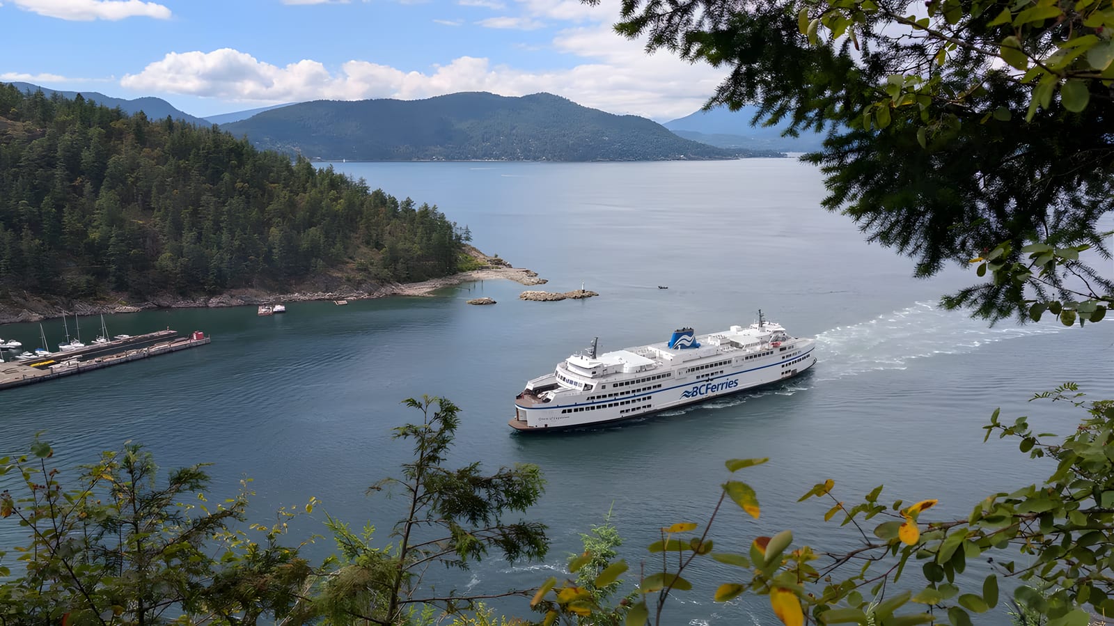 A BC Ferries vessel crossing Howe Sound seen through trees from a bluff.